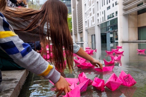 Photo of a child and small pink paper boats floating on water
