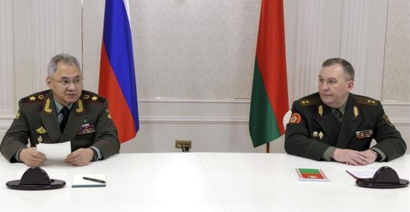 Russian Defence Minister Sergei Shoigu and Belarusian Defence Minister Viktor Khrenin sit behind a desk with their respective countrys flags behind them
