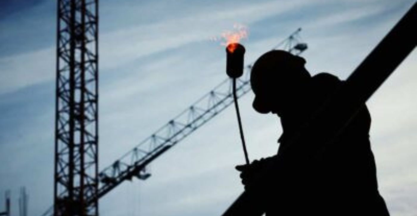 The silhouette of a steel worker in front of cranes 