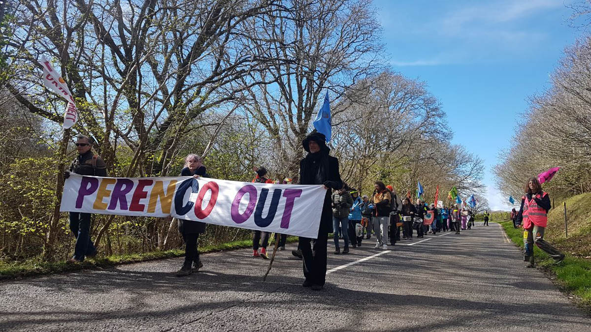 A photo showing people marching down one side of a country road, with three people at the front holding a banner saying Perenco Out