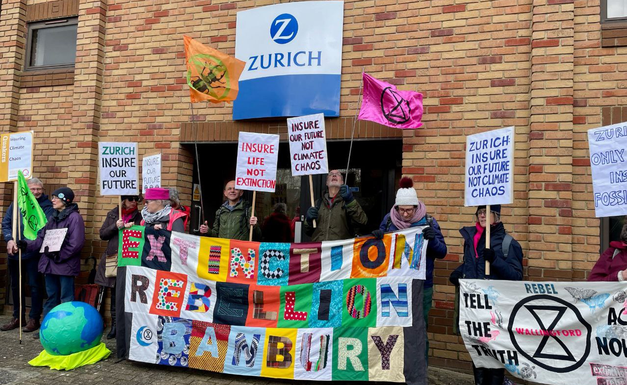 A photo showing people protesting outside the offices of Zurich insurance, holding up placards and in front of a big banner that reads Extinction Rebellion Canterbury