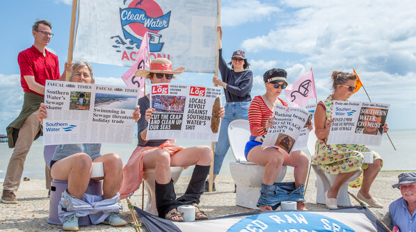 A photo of people sitting on toilets on a beach reading fake newspapers with headlines about water-polluting companies