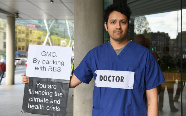 A photo showing a doctor, dressed in blue scrubs, holding a sign saying GMC: By banking with RBS You are financing the climate crisis.