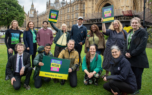 A group of people standing in front of the Houses of Parliament in London holding banners saying 'Restore Nature Now'. Credit: RSPB