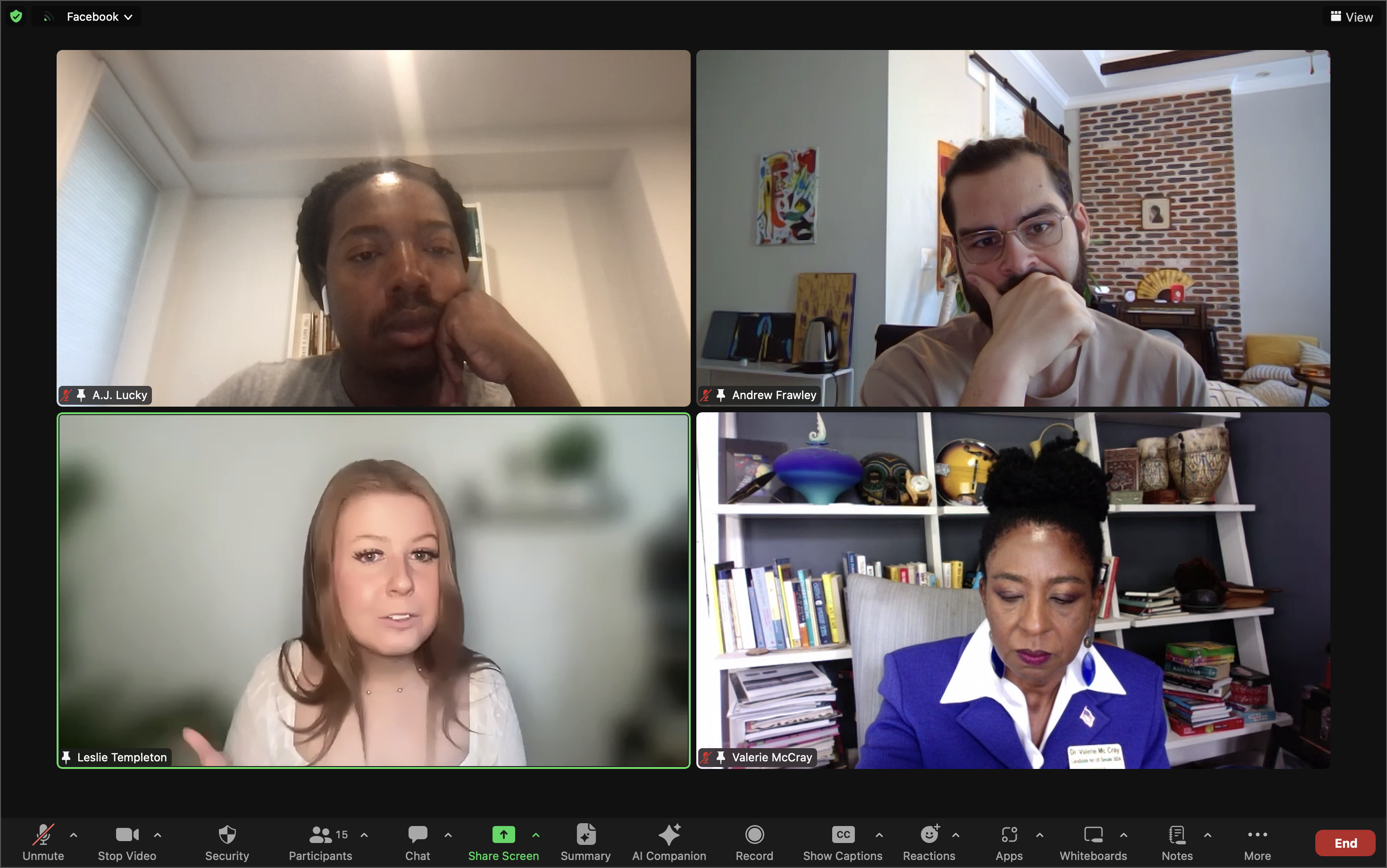  The image is a screenshot of a Zoom video conference with four participants, each in their own video tile. The participants are:  A.J. Lucky: A man with short, curly hair, resting his chin on his hand, wearing a grey t-shirt. He appears thoughtful and is sitting in a room with a white wall and window blinds behind him. Andrew Frawley: A man with glasses, a beard, and a mustache, also resting his chin on his hand. He is in a room with colorful artwork on the wall and a brick wall section behind him. Leslie Templeton: A woman with long, light brown hair, wearing a white top. She is speaking with an expressive gesture, and her background is blurred with some green plants visible. Valerie McCray: A woman with dark hair styled in a bun, wearing a blue blazer and a white shirt. She appears focused and is seated in front of a bookshelf filled with books and various decorative items. The Zoom interface shows typical features such as participant names, mute status, and meeting controls at the bottom.