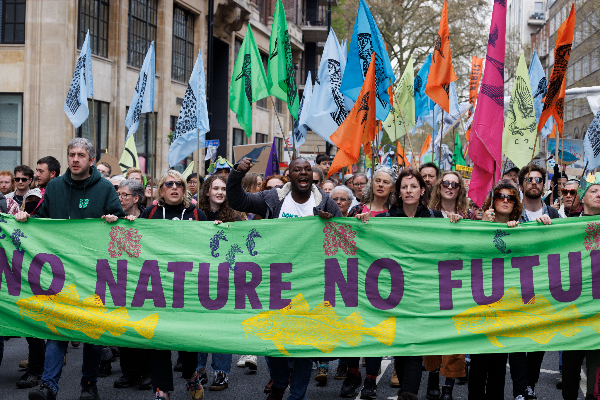 A group of people marching in front of a green banner which says No Nature No Future