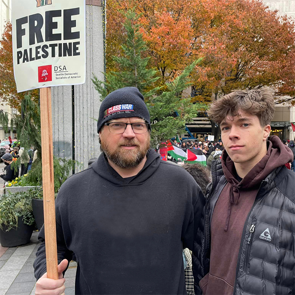 A photo of Jason and his son at a Palestinian solidarity protest in Seattle. Jason is holding a sign that says “Free Palestine.”