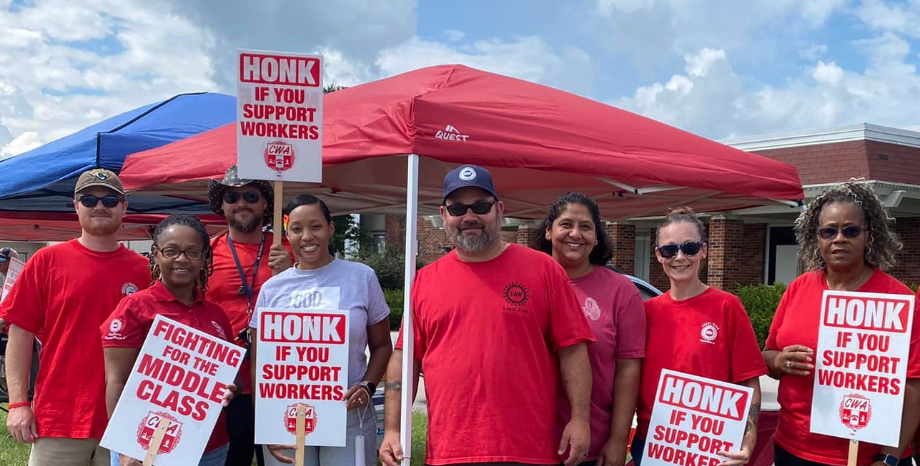 A photo of AT&T workers with a sign reading, “Honk If You Support Workers.”