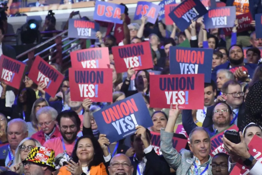 A crowd of people at the Democratic National Convention in August hold signs in magenta and navy blue that read 