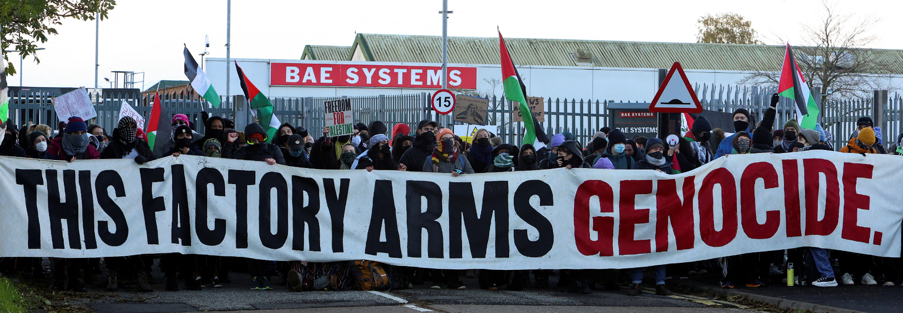 Protesters outside of BAE Systems holding Palestinian flags and a large banner reading 