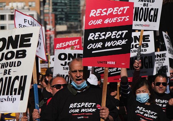 A photo of striking hotel workers with signs that read, “Respect Our Guests, Respect Our Work.”