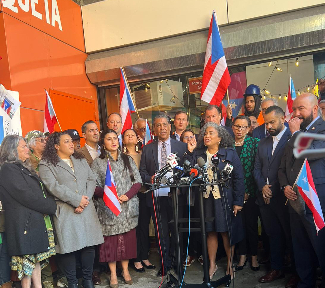 Elected Officials Stand at a press conference, holding Puerto Rican Flags.