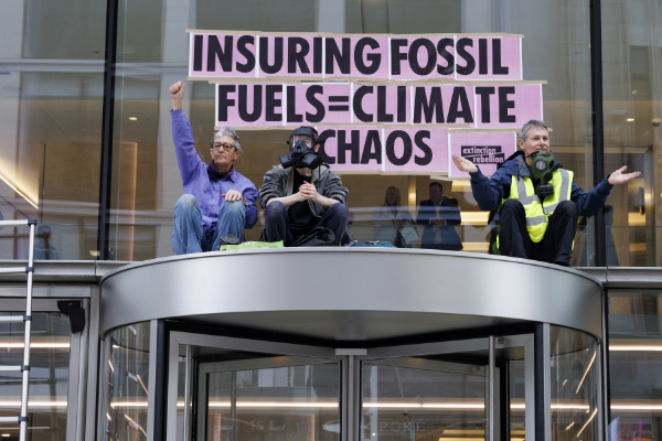 three rebels on top of lobby entrance roof with pink paper sign stuck on window saying insuring fossil fuels = climate chaos