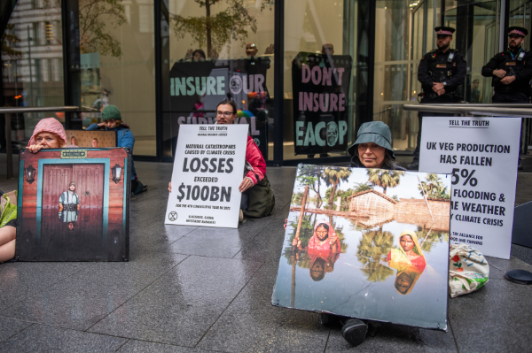 people sitting in front of the 'Gherkin' building with large photos of flood disasters