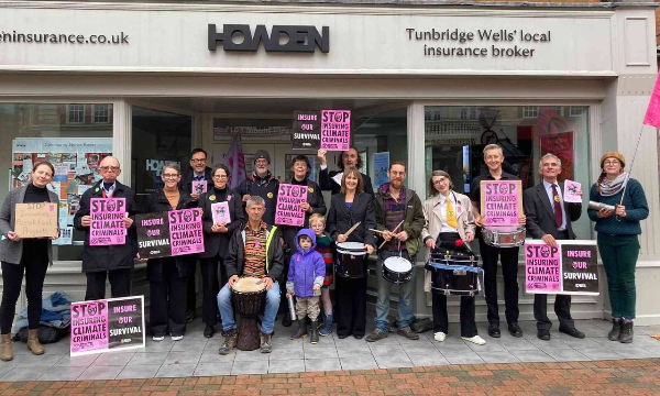 three rebels on top of lobby entrance roof with pink paper sign stuck on window saying insuring fossil fuels = climate chaos