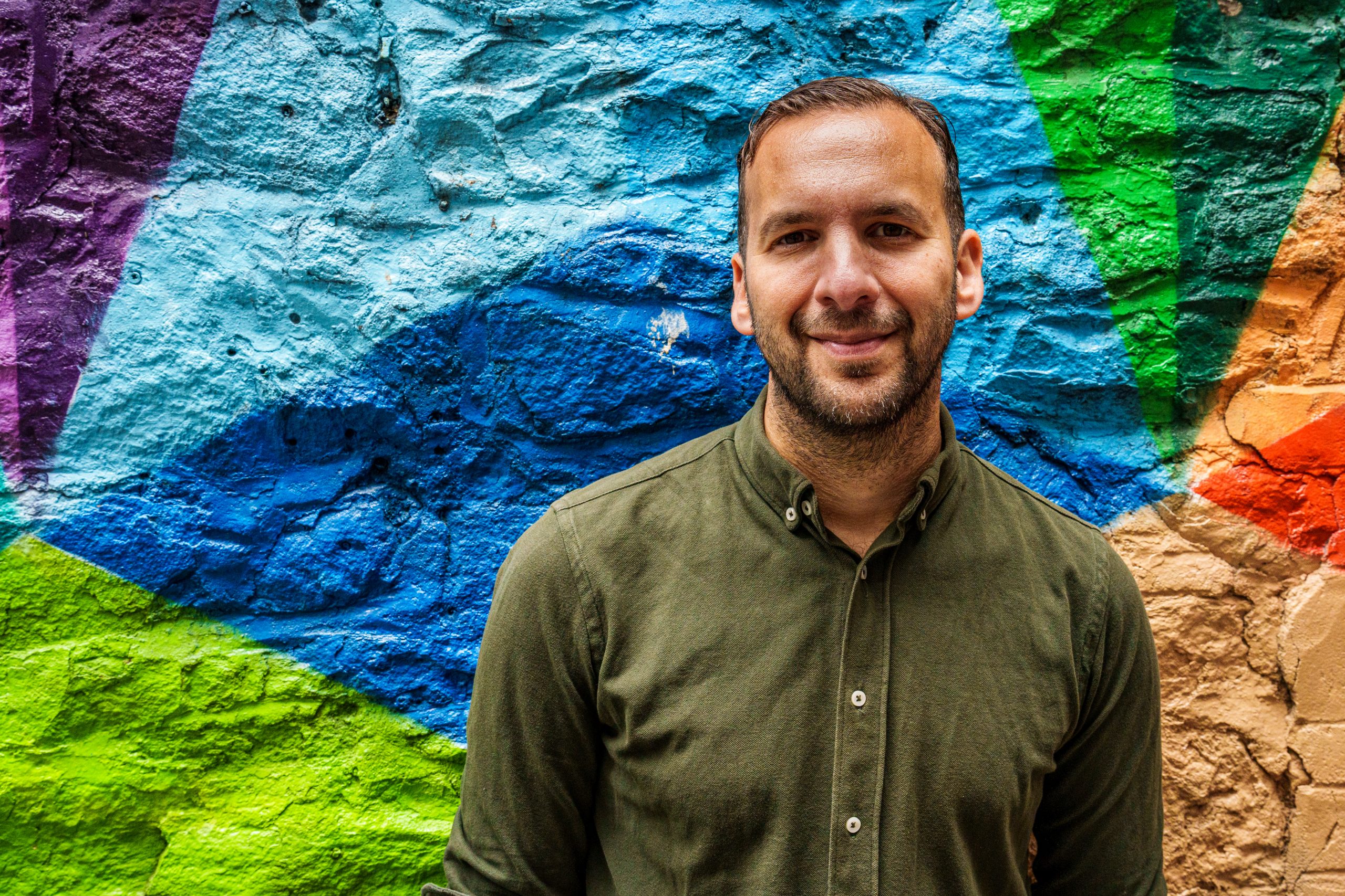 Deputy leader Zack Polanski in front of a colourful wall.