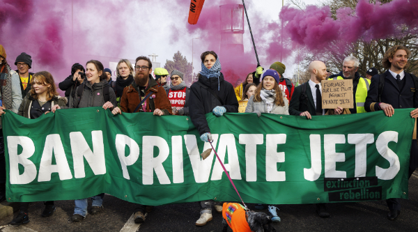 Ban Private Jets green banner with rebels and pink smoke behind