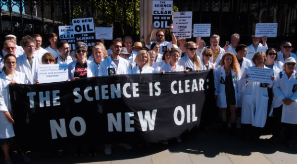 Scientists in white lab coats holding black banner with white letters reading 'The science is clear - no new oil'