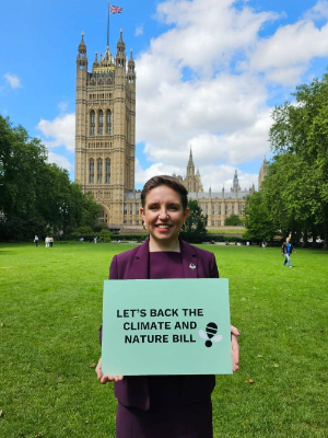 Carla Denyer standing in front of Westminster with a poster that says 'Let's back the climate and nature bill'.