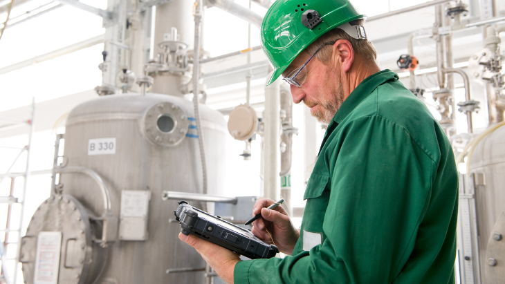 A middle-aged industrial worker in stands in front of equipment while checking his clipboard