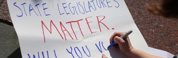 A protestor finishing a poster that highlights the significance of state legislatures.