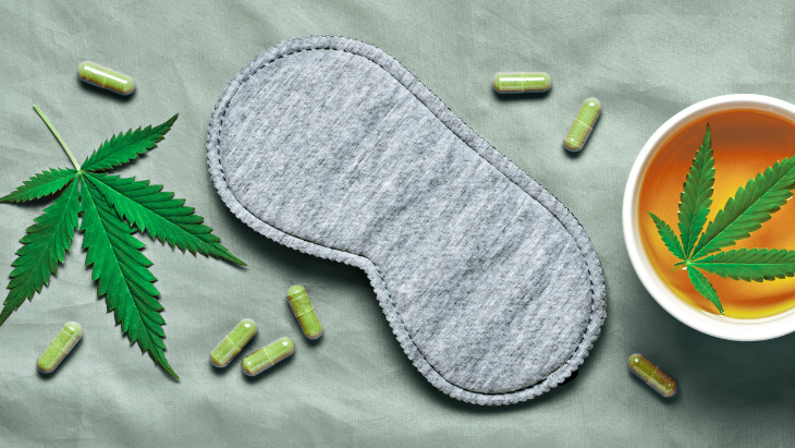 a cannabis leaf, capsules, eye mask for sleeping, and a teacup filled with tea with cannabis leaf floating in it, are on a bed sheet
