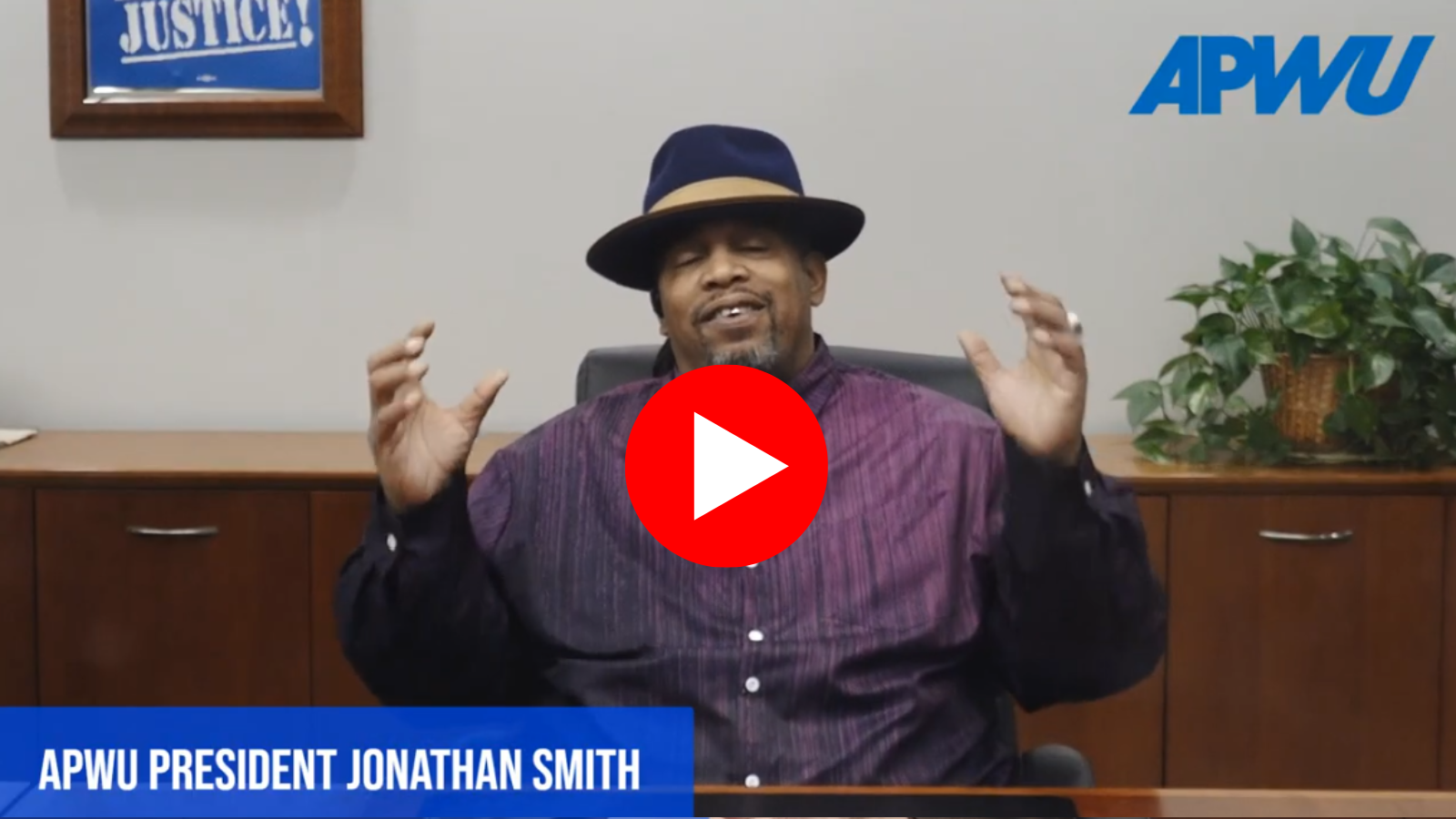 Screengrab from Youtube of APWU President Mark Dimondstein at a desk with a plant behind him, delivering his final address as APWU president. 