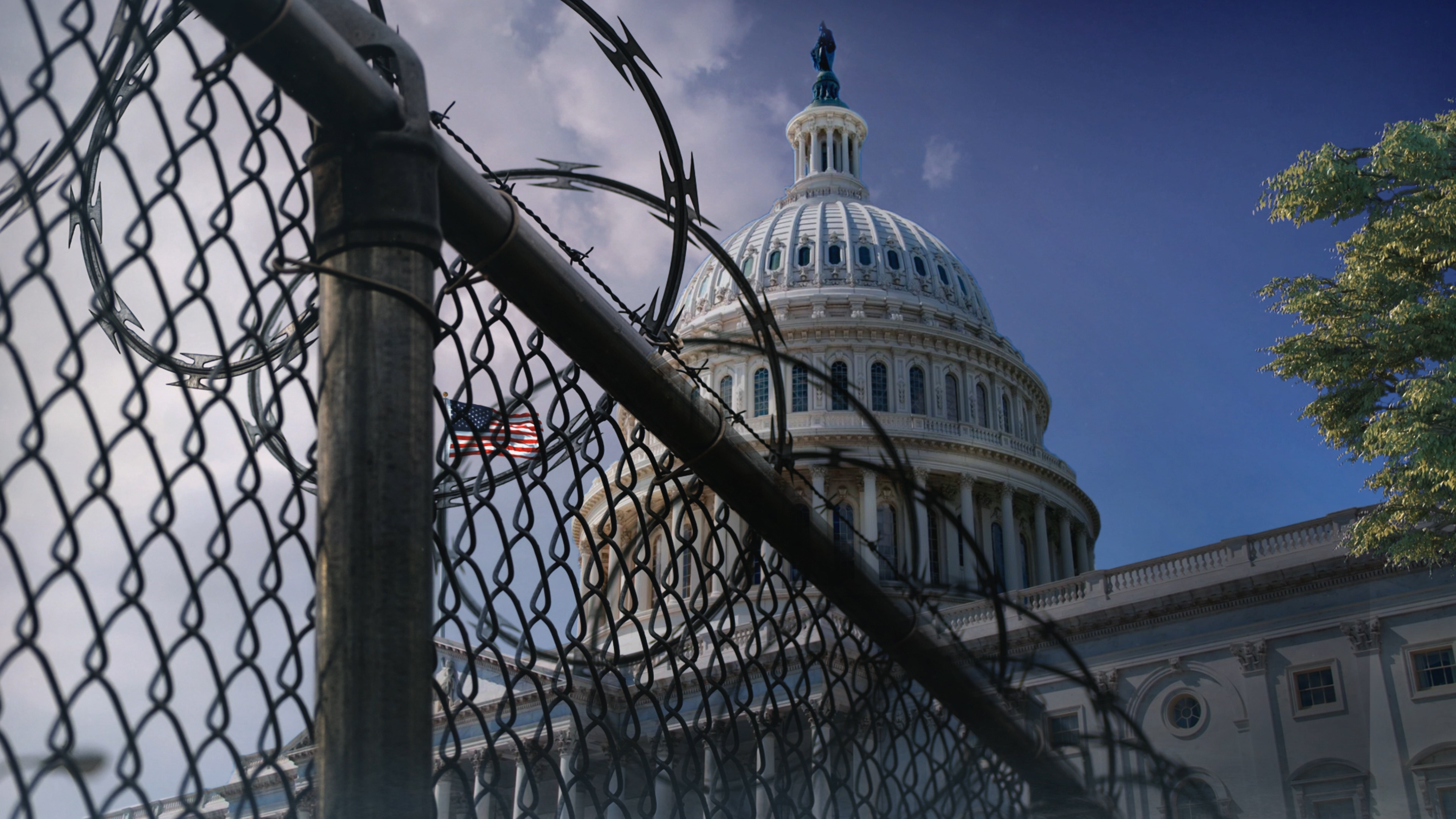 A view of the U.S. Capitol Building at an angle behind razor wire fencing with clouds in the background.