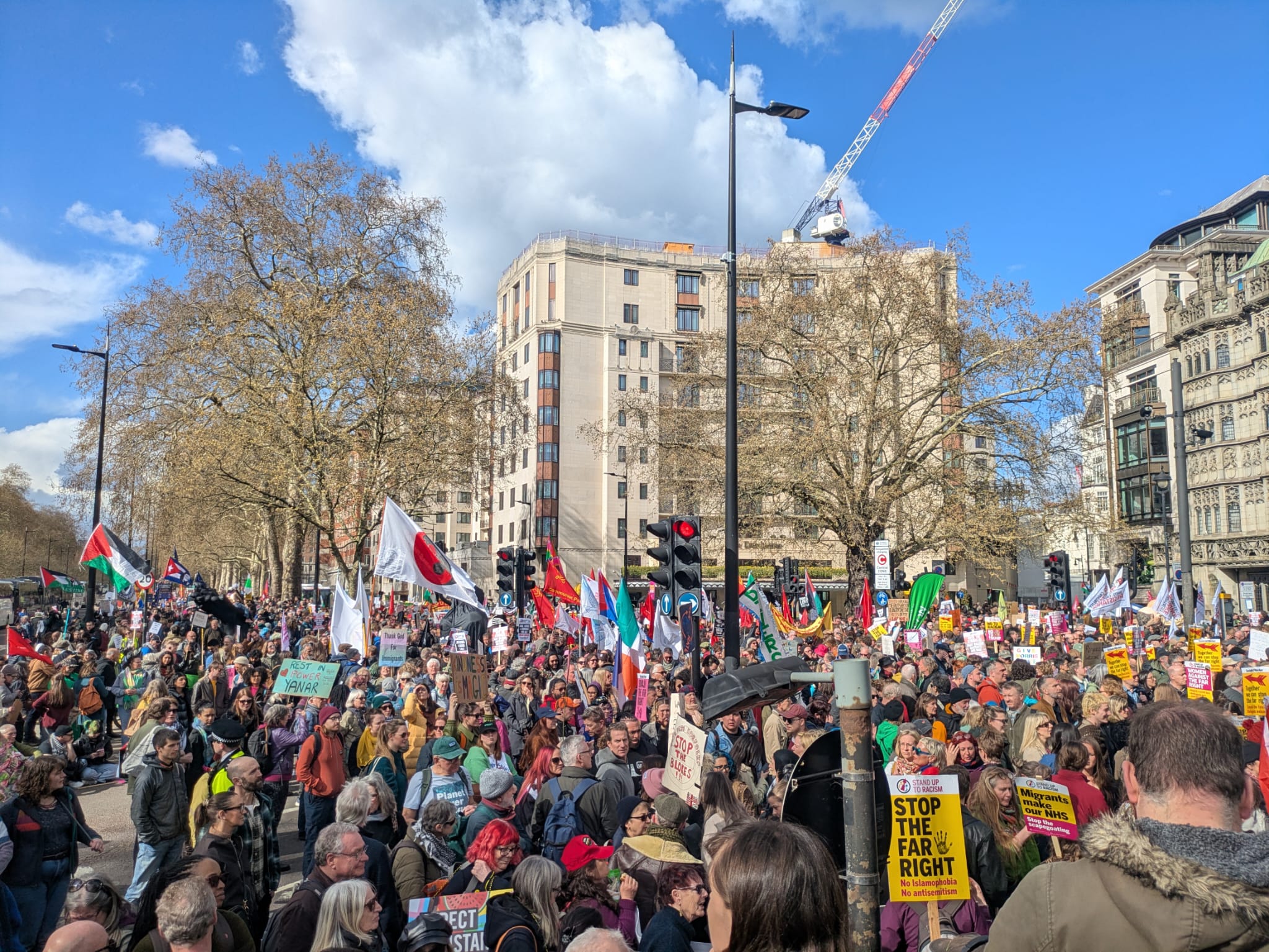 [very crowded street on sunny day with flags and placards]