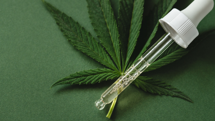 a dropper of cannabis oil with a cannabis leaf in the background