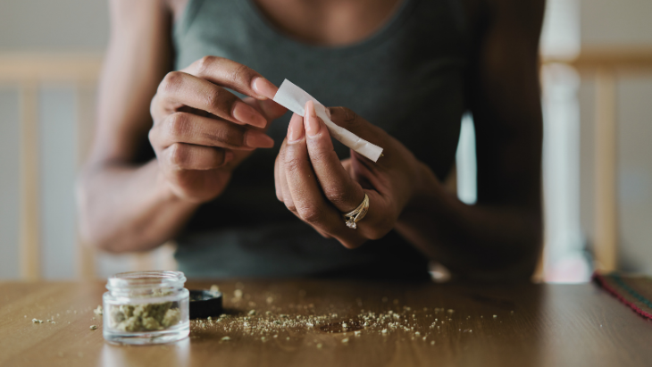 a woman seated at a table rolls a legal cannabis joint