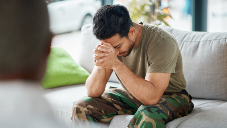 a disappointed veteran seated on a couch rests his hands against his clasped hands