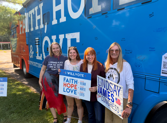 A photo of Iowa congressional candidate Lindsay James and supporters in front of the Faith, Hope, & Love bus.