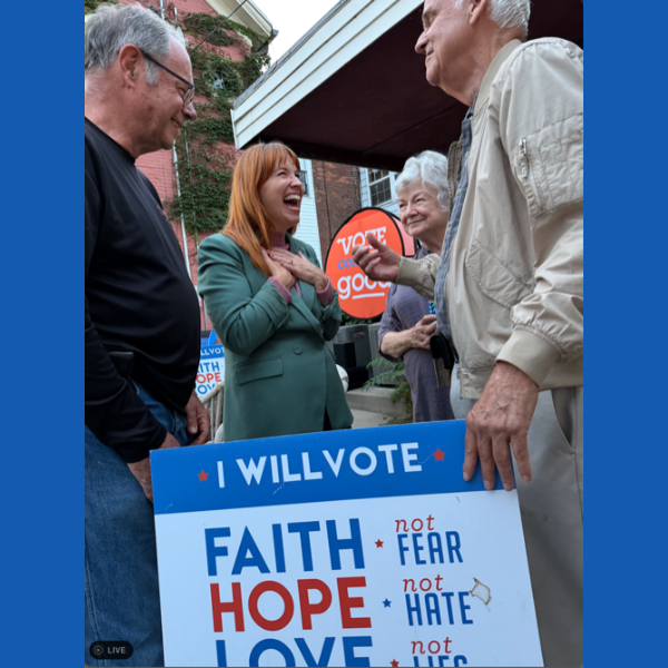 A photo featuring Lindsay James, running in Iowa's 2nd District, standing behind a Vote Common Good sign.