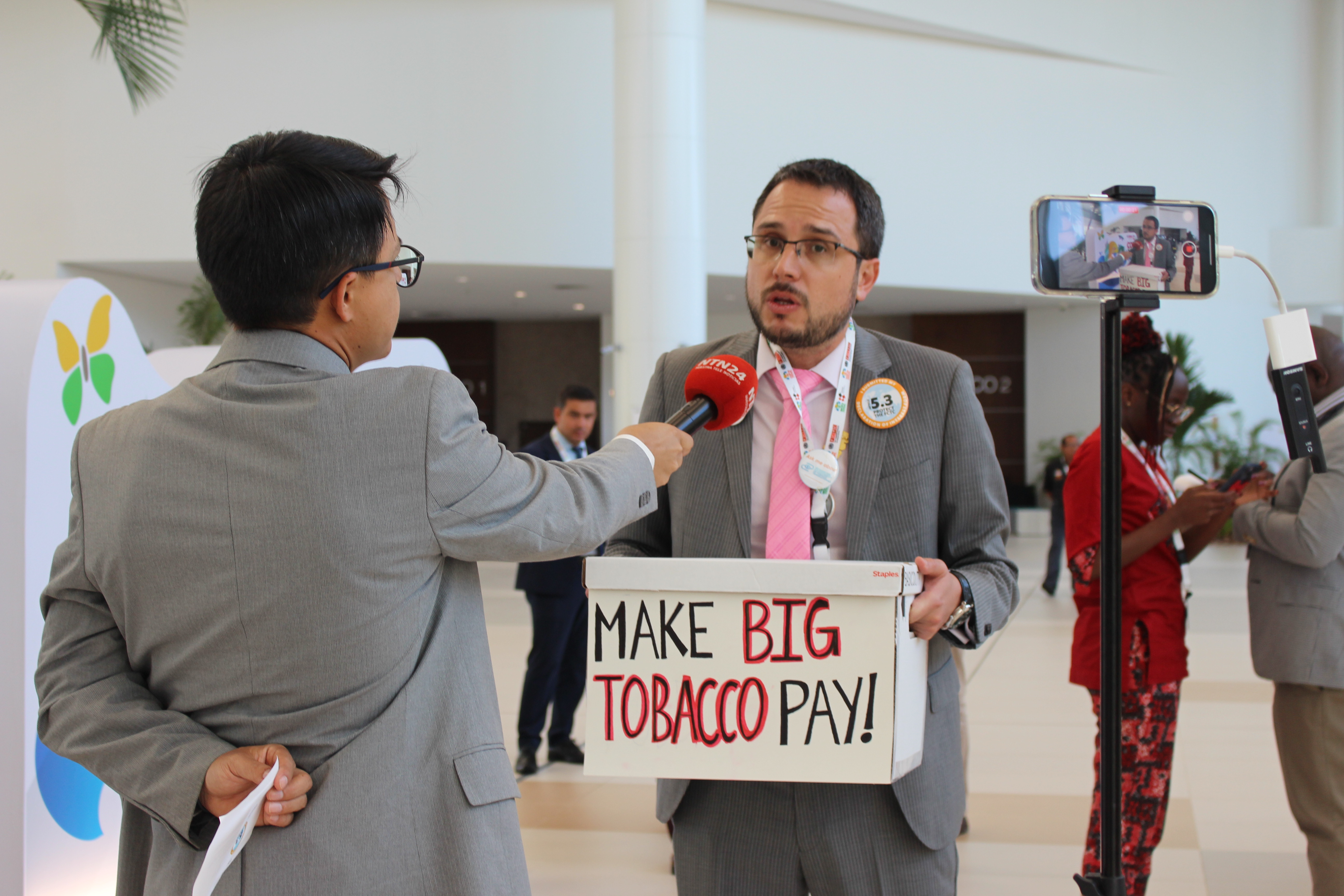 Tobacco Campaign Director Daniel Dorado holding a sign that says 'Make Big Tobacco Pay' while giving an interview at last year's global tobacco treaty negotiations.