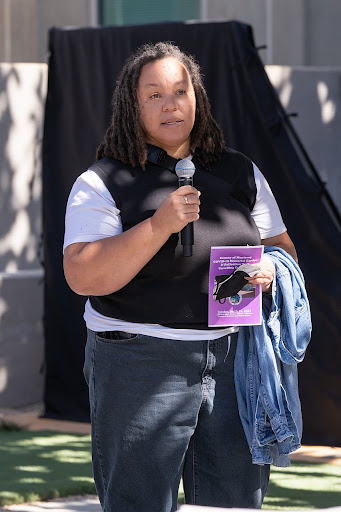 Hilary Porter speaks at a microphone at the Monterey County COVID-19 Memorial unveiling, holding a program for the event.